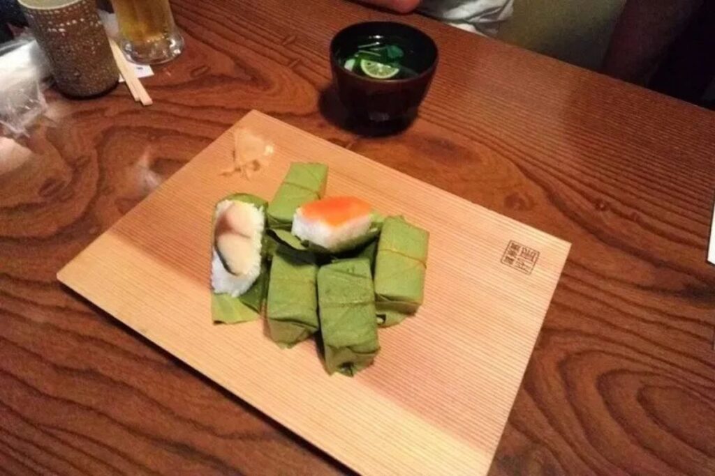 Traditional regional sushi wrapped in green persimmon leaves served on a wooden block platter.
