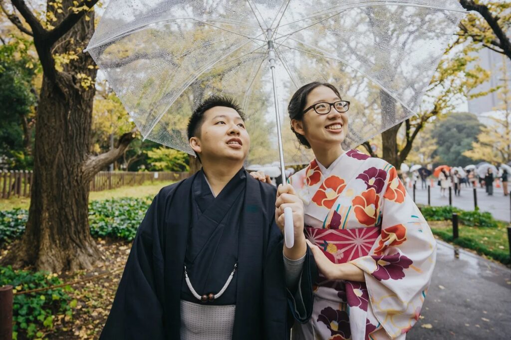 Couple in kimono posing with a clear umbrella under autumn ginkgo trees in Tokyo