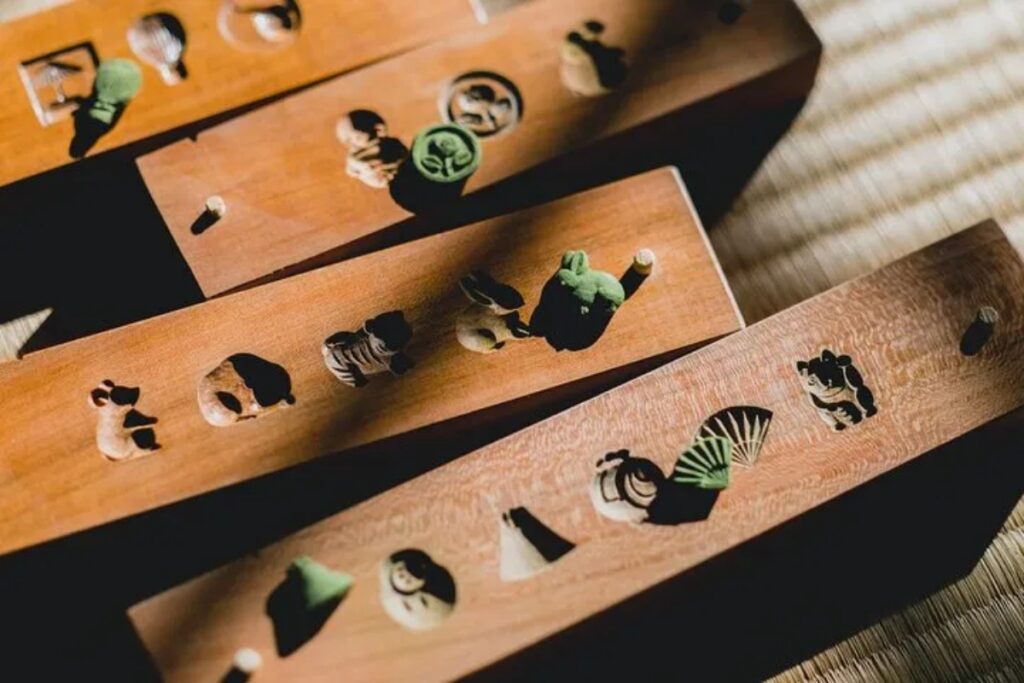 Rhythmic wooden confectionery molds basking in natural light inside a quiet temple hosting the Uji matcha incense workshop.