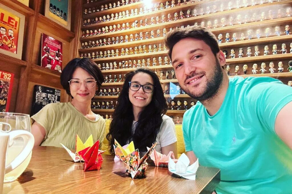 Happy international tourists and their local guide smiling with completed paper cranes inside a cozy venue for a Tokyo origami private workshop.