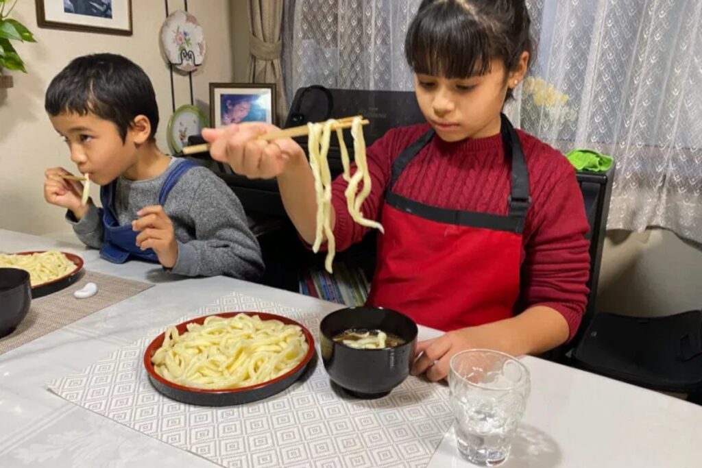 Children happily eating their handmade udon noodles with chopsticks at a Japanese family home