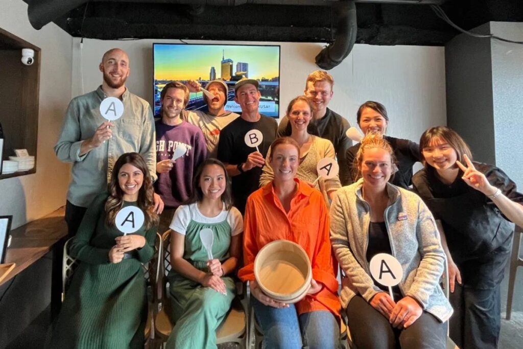 Large group of guests posing with rice paddles at a fun Tokyo sushi making experience in Asakusa