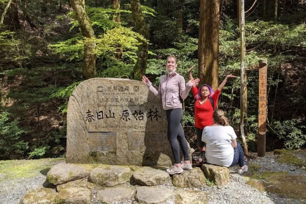 Two individuals posing next to an old stone monument marker deep within a lush woodland.