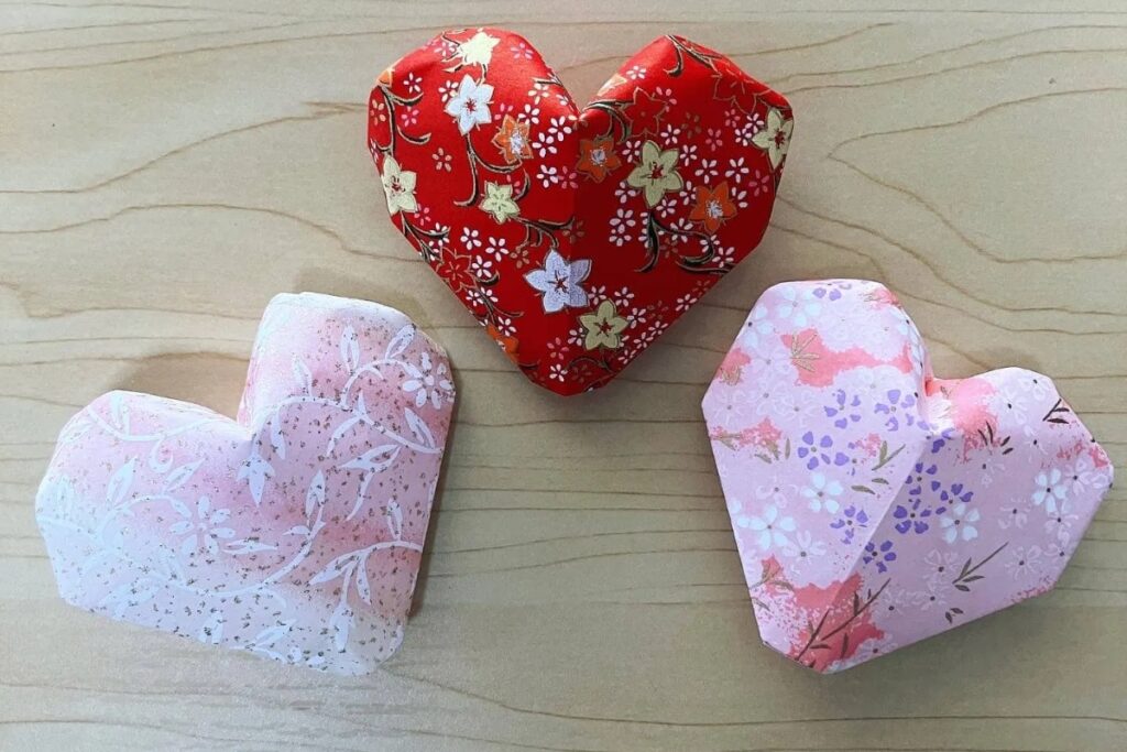 Three beautifully sculpted, three-dimensional origami hearts made from traditional floral patterned paper at a Tokyo origami private workshop.