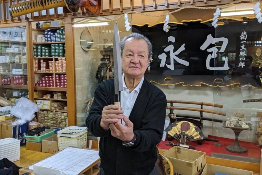 A professional craftsman proudly displaying a finely crafted steel blade in his traditional storefront.