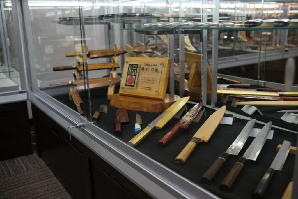 High-quality culinary blades displayed beautifully in a glass case on a Sakai knife factory tour.