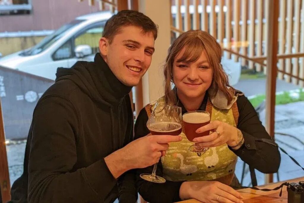 A smiling couple holding up glasses of refreshing craft beer.