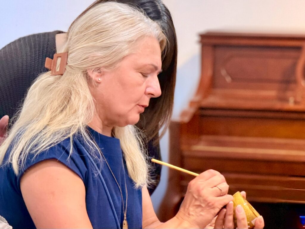 A close-up view of a participant delicately dusting gold powder onto a repaired ceramic bowl during a traditional Kintsugi workshop in Ginza.