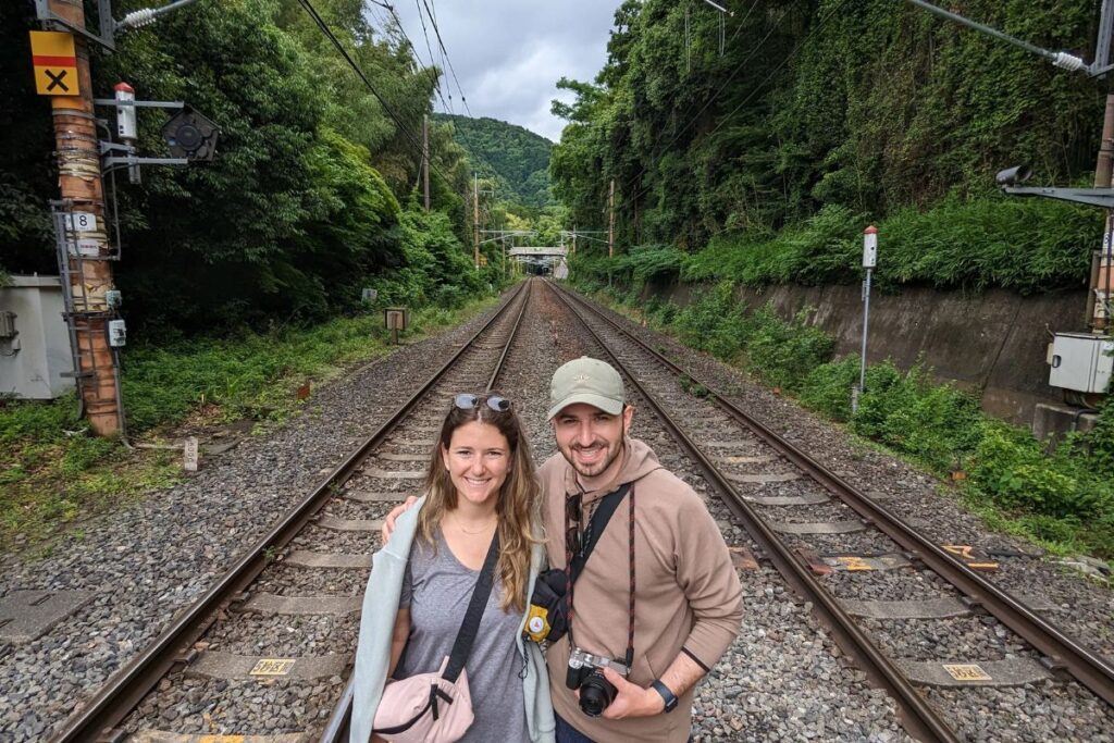 A happy couple posing together on scenic railway tracks surrounded by lush green forest.