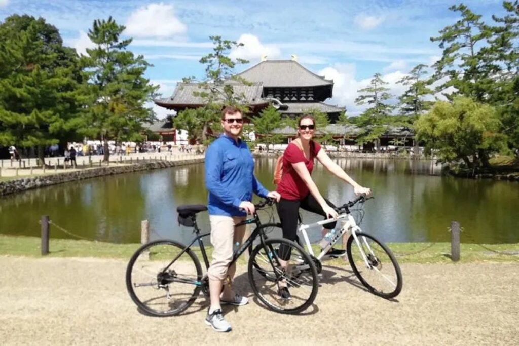 A couple posing with their bicycles in front of a grand temple during a Nara highlights bike tour.