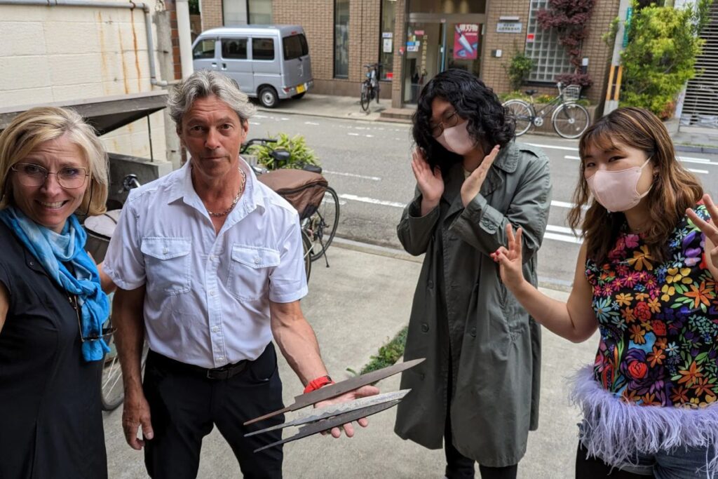 Travelers smiling while holding raw steel blades outside on a private sakai knife tour.