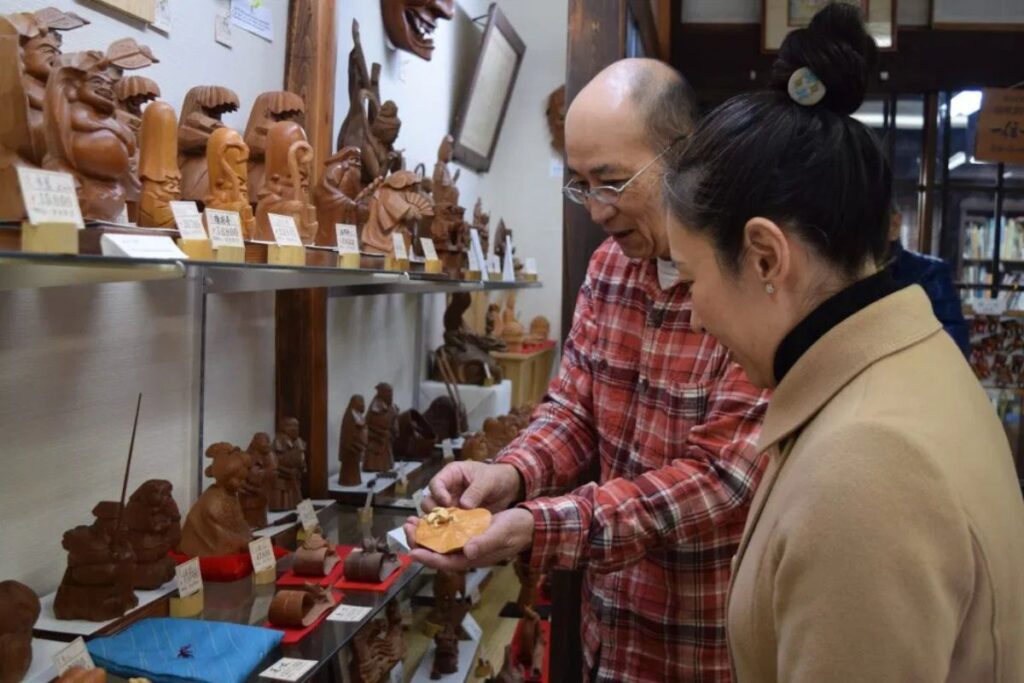 An artisan demonstrating traditional wood carving techniques to guests inside a local workshop on a Takayama craft tour.
