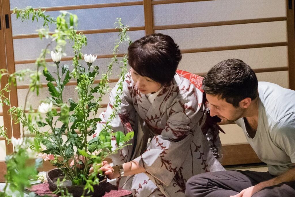 A male student watching closely as an instructor in a traditional kimono adjusts a floral design during a Kyoto Machiya Ikebana class.