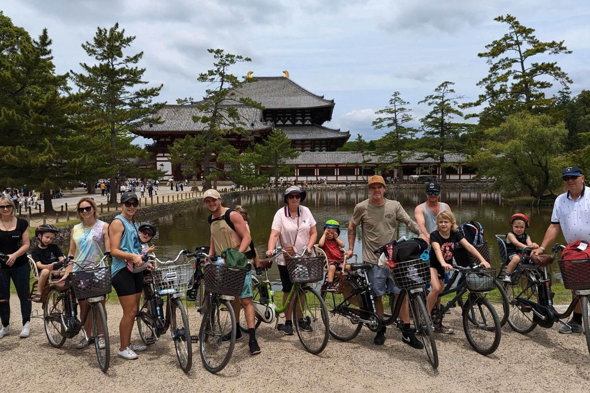 A large mixed group of adults and children posing with their electric two-wheeled vehicles during a private nara e-bike tour.