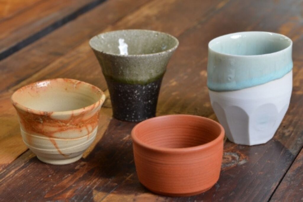 A collection of four distinct, handcrafted Tokoname-yaki pottery cups from the "Sasara-ke" set, used during the premium sake tasting experience.