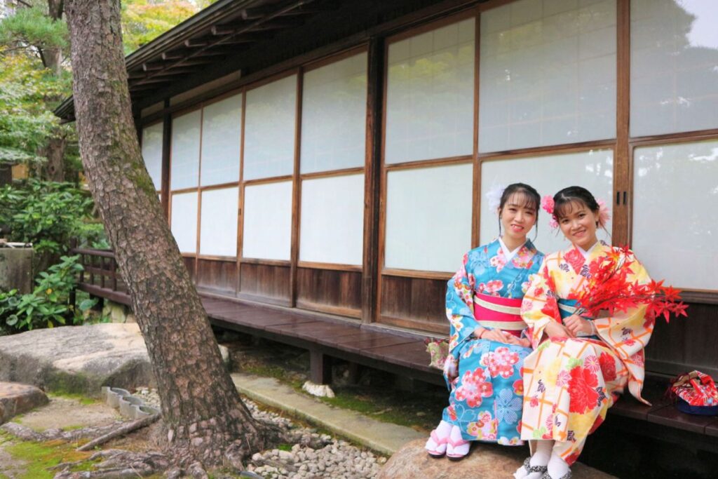 Two guests smiling on a wooden engawa bench outside traditional shoji doors during the Kimono and matcha experience Nagoya.