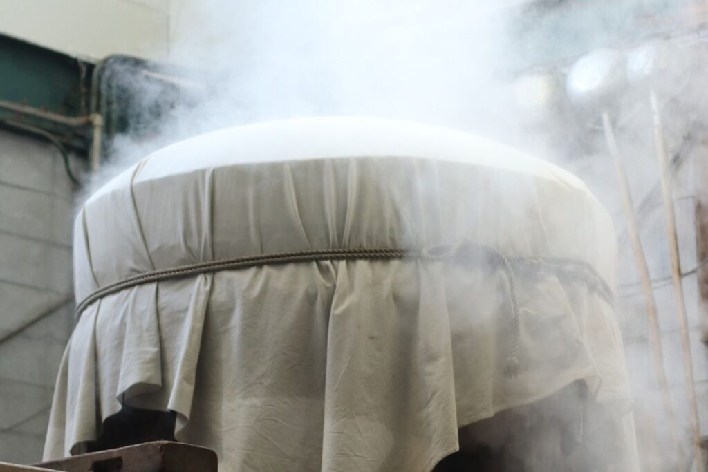 Freshly steamed rice rising from a traditional koshiki vat inside the brewery