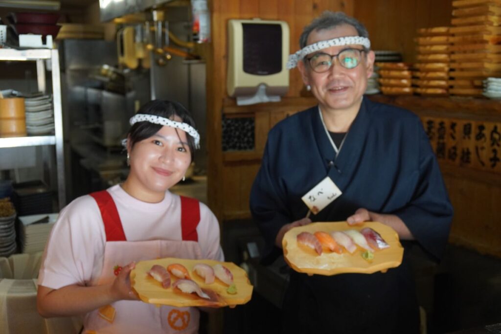 A smiling guest and a 30-year veteran master chef proudly displaying freshly made nigiri during a hands-on Nagoya sushi making class.