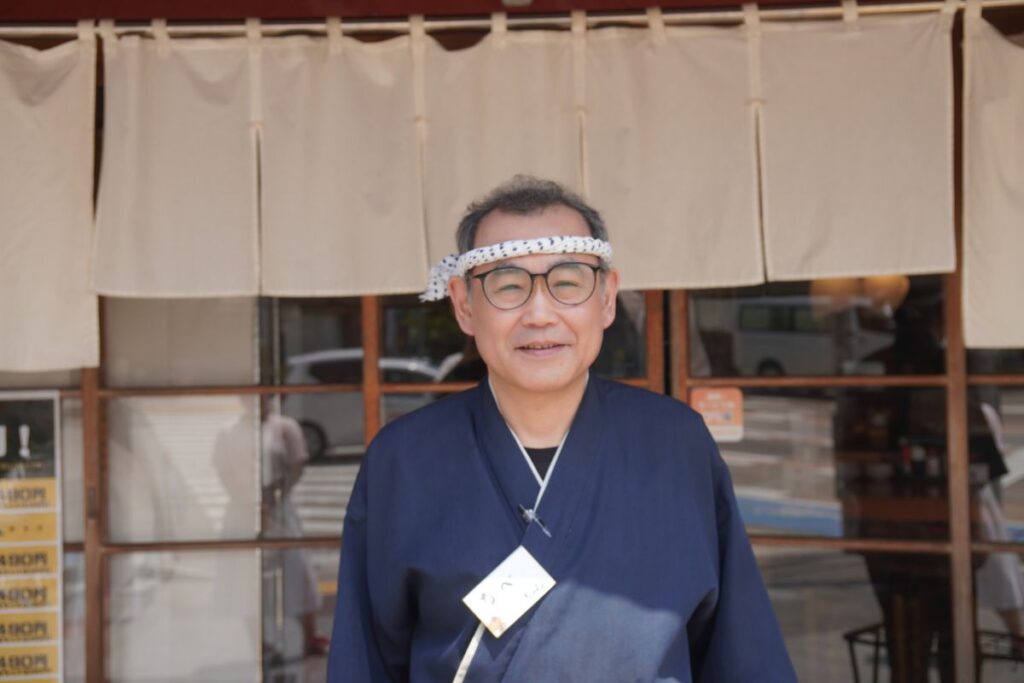Our 30-year veteran master chef smiling in front of the traditional curtain entrance of the venue before a Nagoya sushi making masterclass.