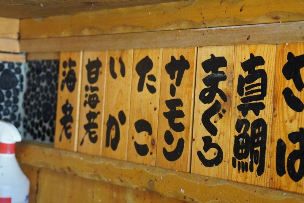 Traditional Japanese hand-painted wooden menu boards hanging above the kitchen counter at the Nagoya sushi making workshop.