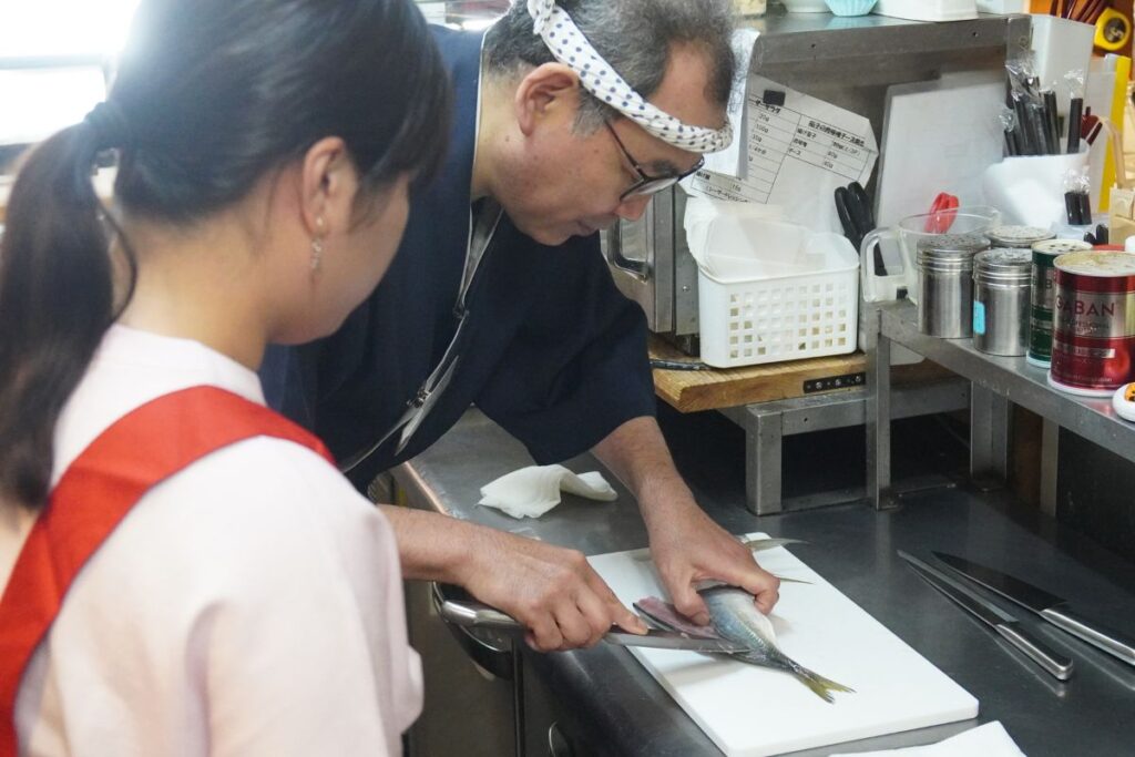 A master chef showing a student how to correctly hold the knife to execute the classic sanmai-oroshi filleting method in a Nagoya sushi making lesson.