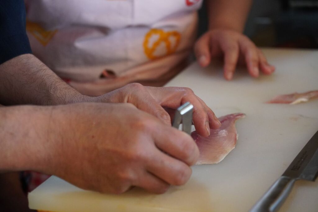 Using specialized Japanese fish tweezers to delicately remove tiny pin bones from a fresh fillet during a Nagoya sushi making class.