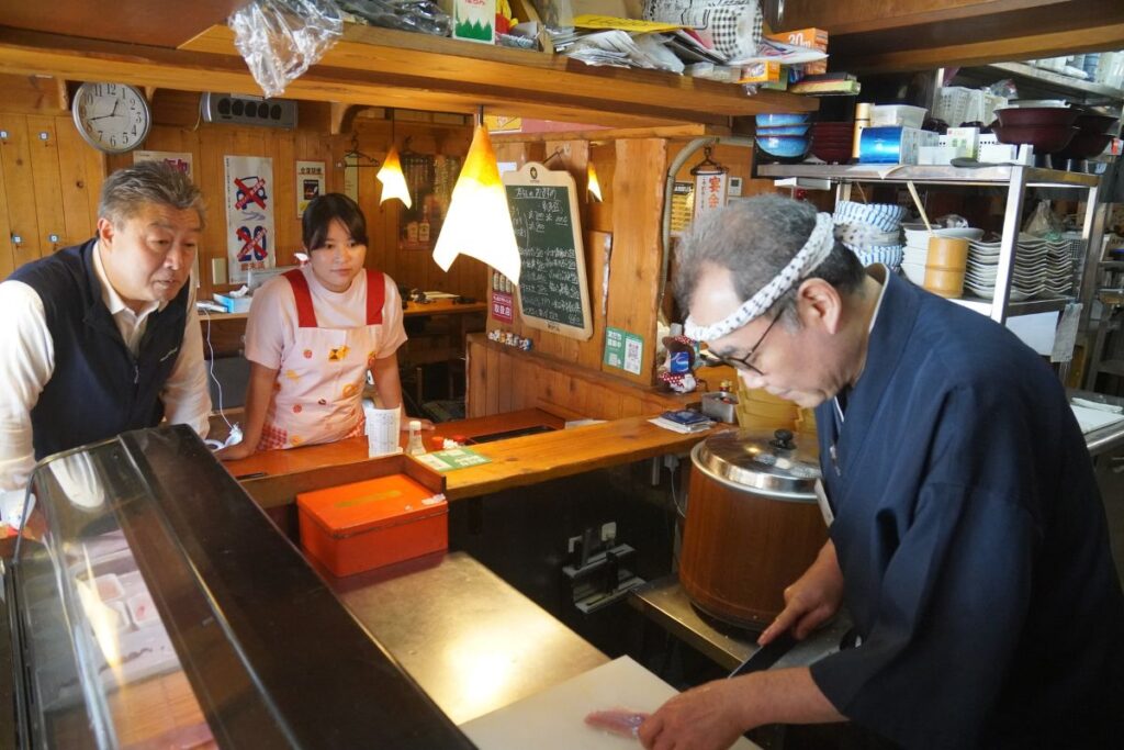 An overview of the authentic sushi restaurant kitchen as guests watch the veteran master chef demonstrate professional preparation techniques.