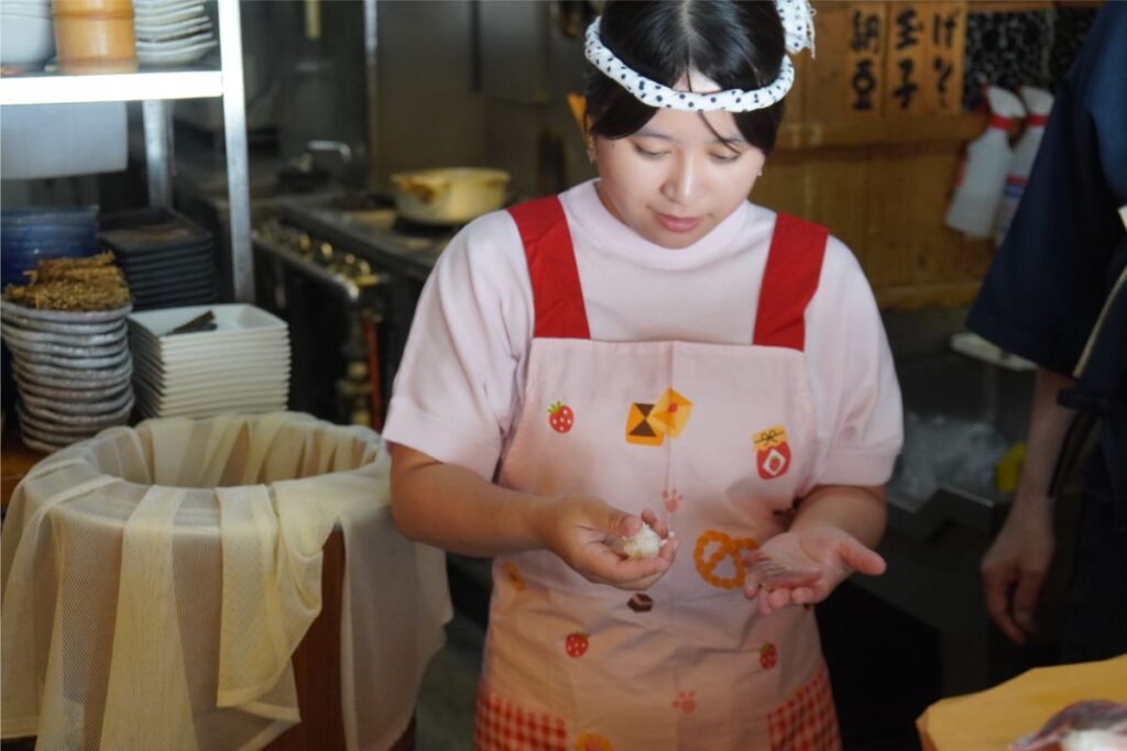 A student wearing a traditional headwear learning how to gently press and shape the seasoned shari rice for nigiri.