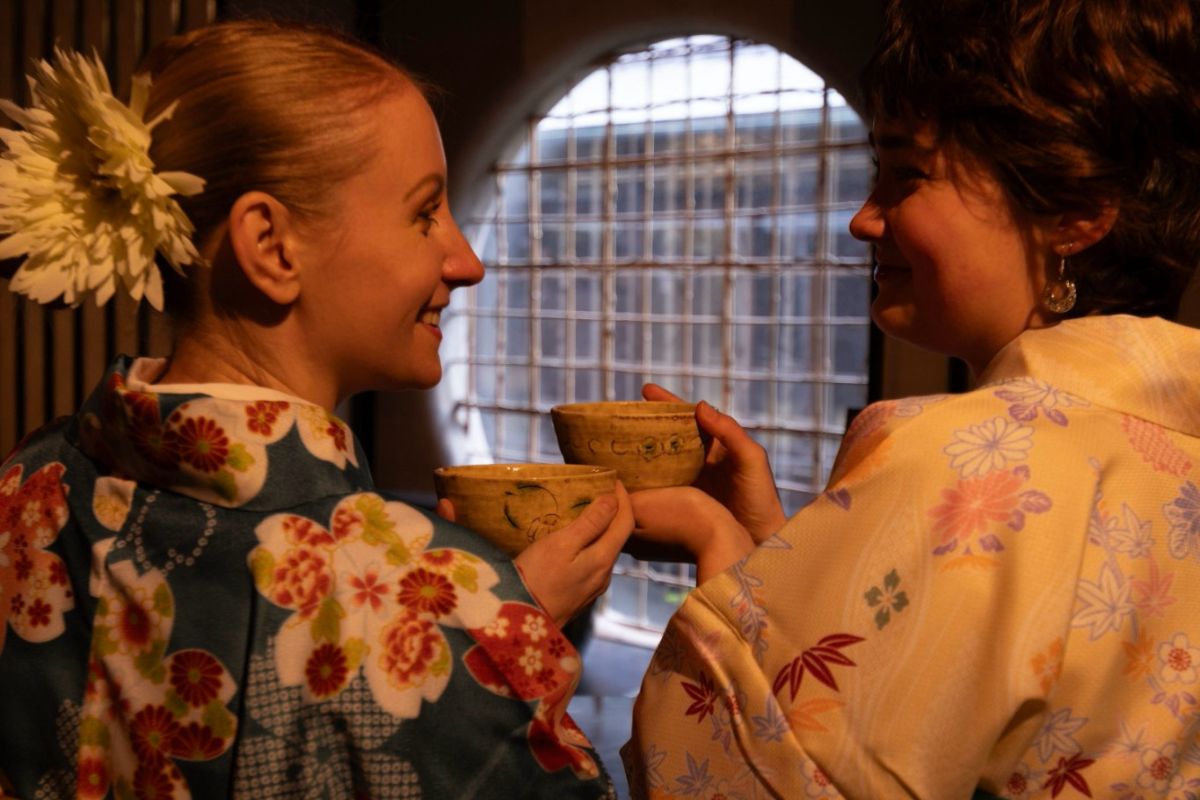 Two women wearing authentic floral kimonos smiling and holding matcha bowls during a private tea experience at the historic Furukawa Art Museum Annex in Nagoya.